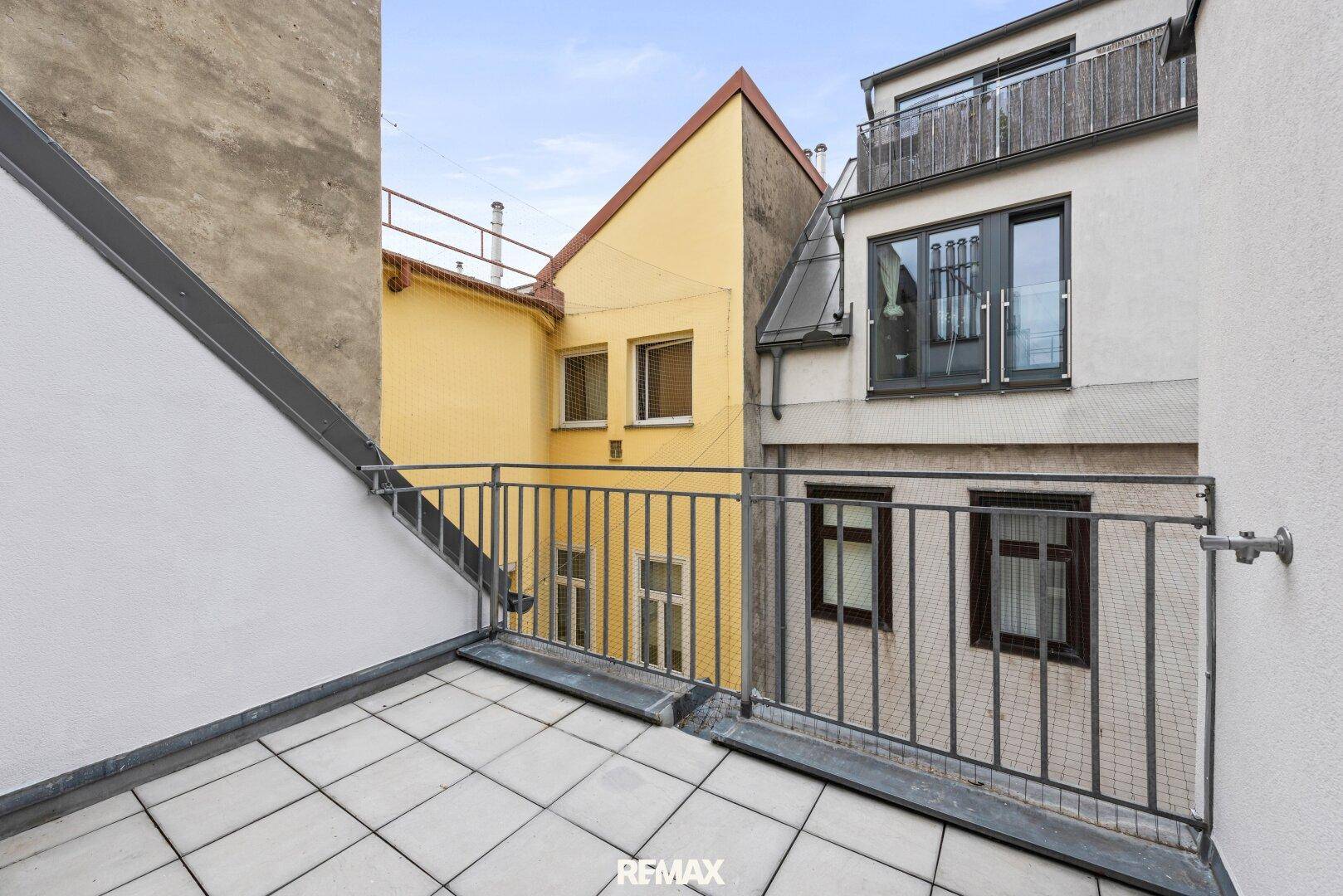 Kleiner Balkon mit Fliesenboden und Blick auf die umliegenden Gebäude.