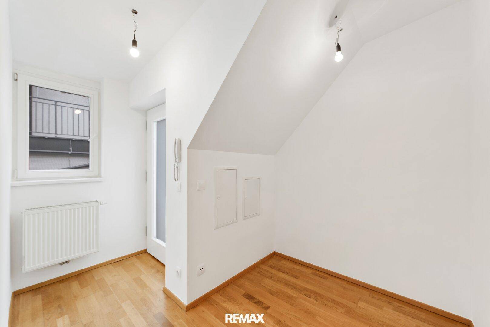 Heller Eingangsbereich mit Holzboden, Fenster und Gegensprechanlage.