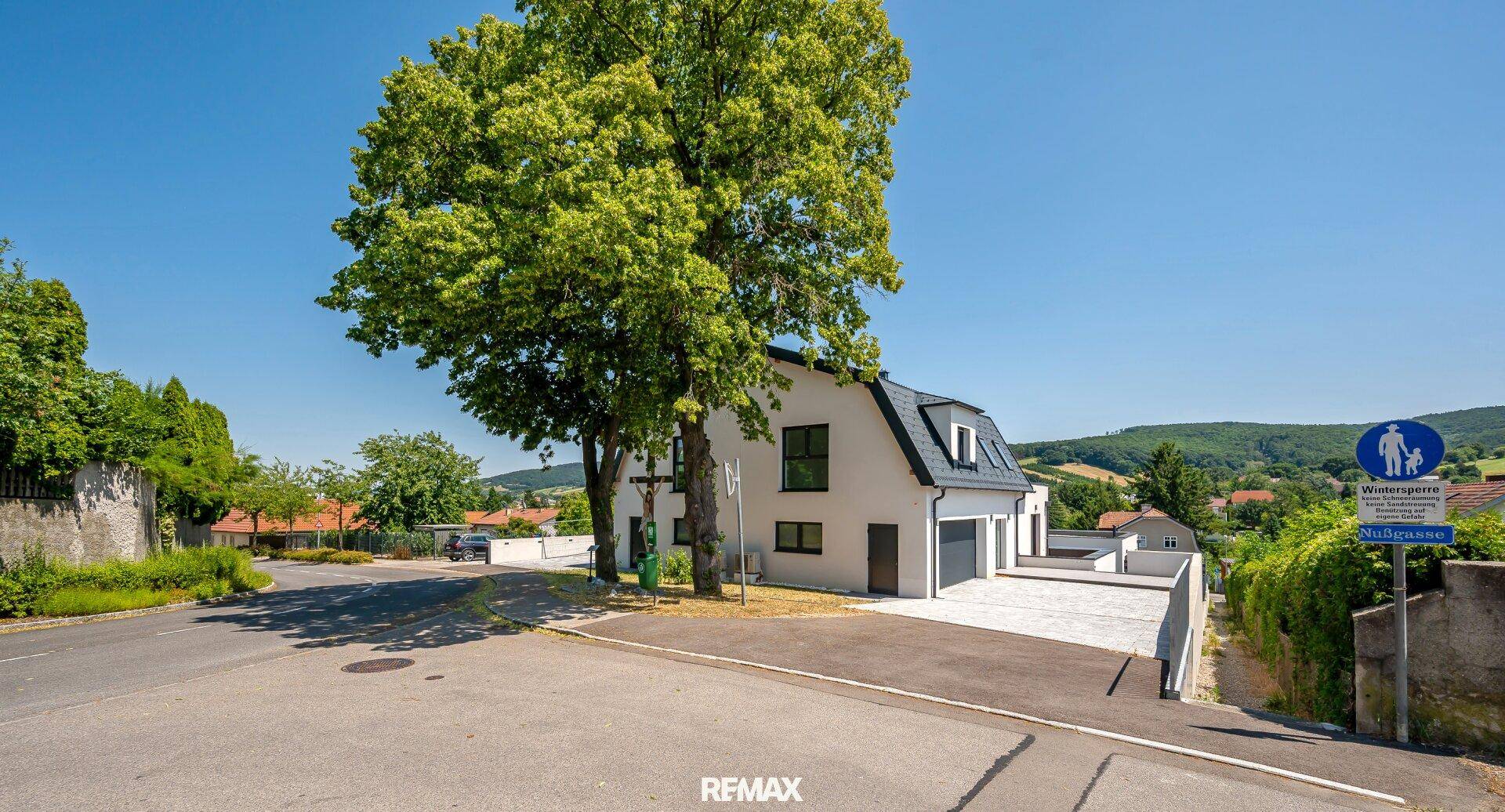 Ansicht des modernen Einfamilienhauses von der Straße mit Zufahrt und Parkplatz.