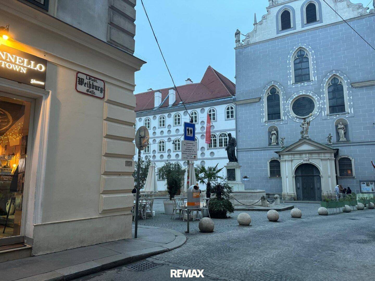Historische Gebäude und ein Platz mit Außengastronomie in einer europäischen Stadt am Tag.