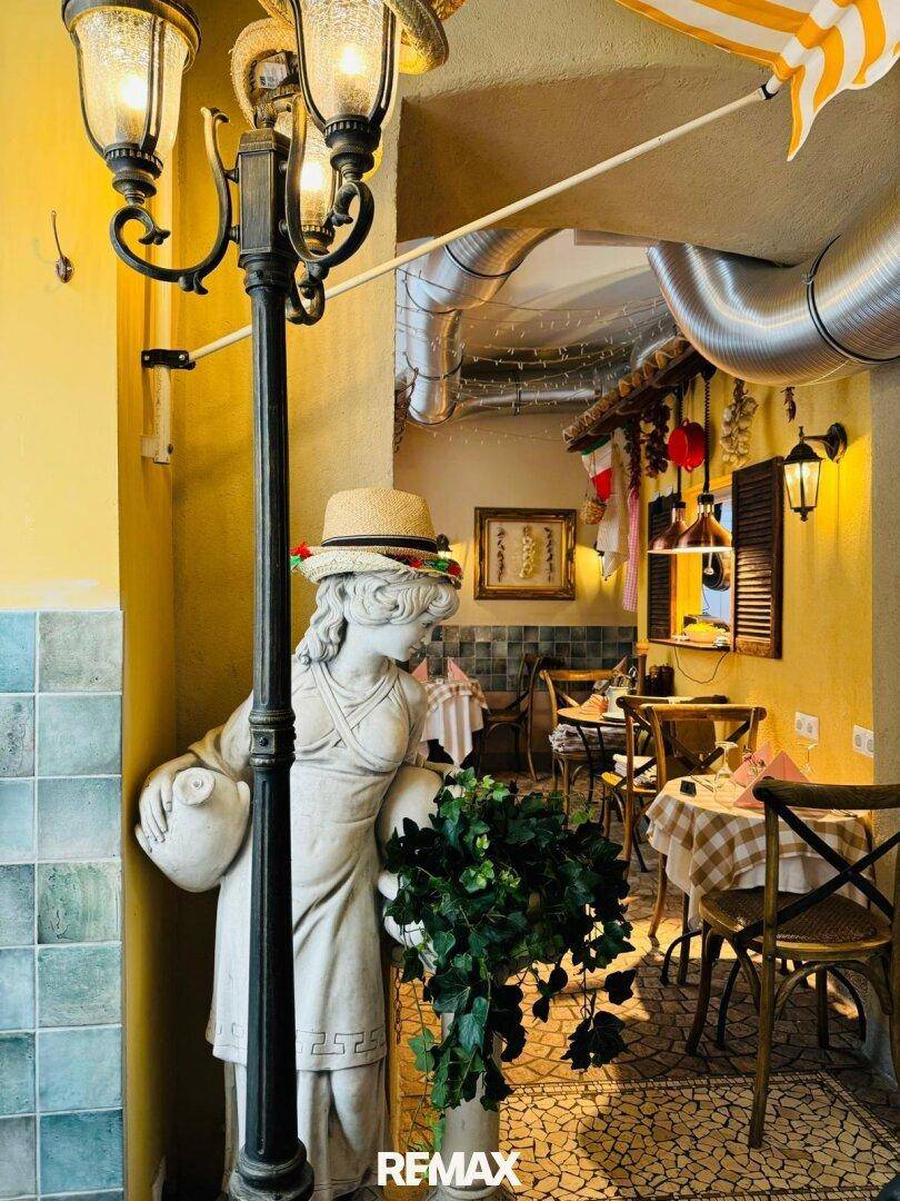 Detailansicht eines Restaurants mit einer Statue, einer Laterne und karierten Tischdecken in warmem Ambiente.