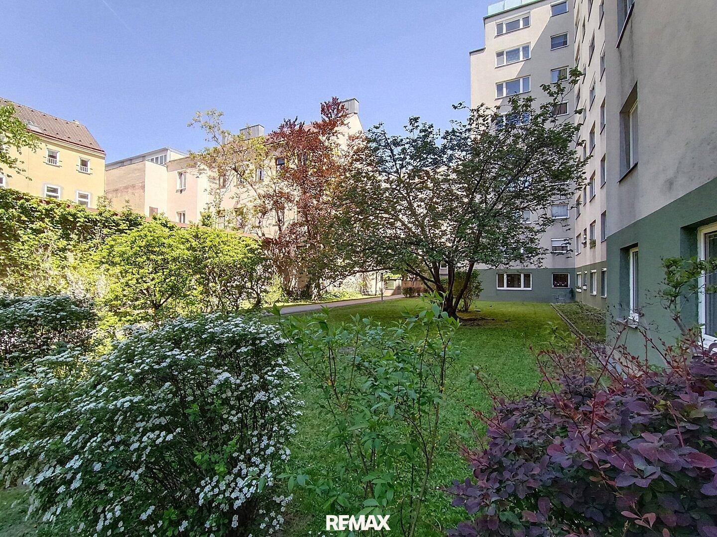 Weitläufiger Gemeinschaftsgarten mit vielfältiger Bepflanzung und altem Baumbestand.