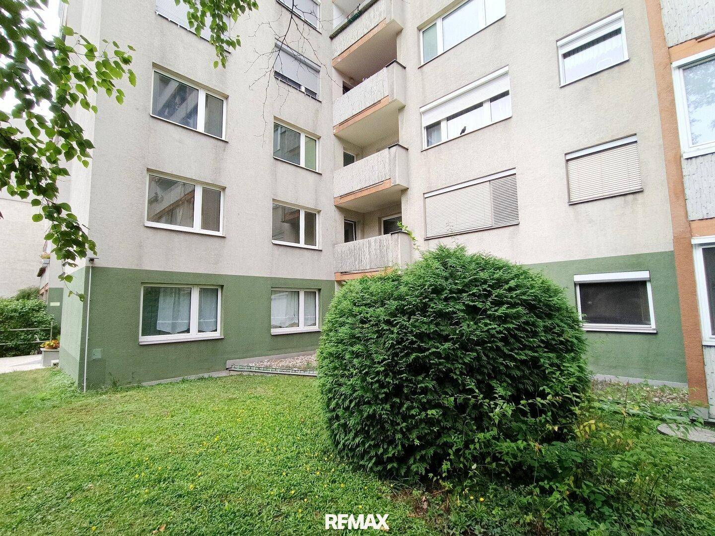 Gebäudefassade mit Balkonen und einem gepflegten Vorgartenbereich, umgeben von Grün.