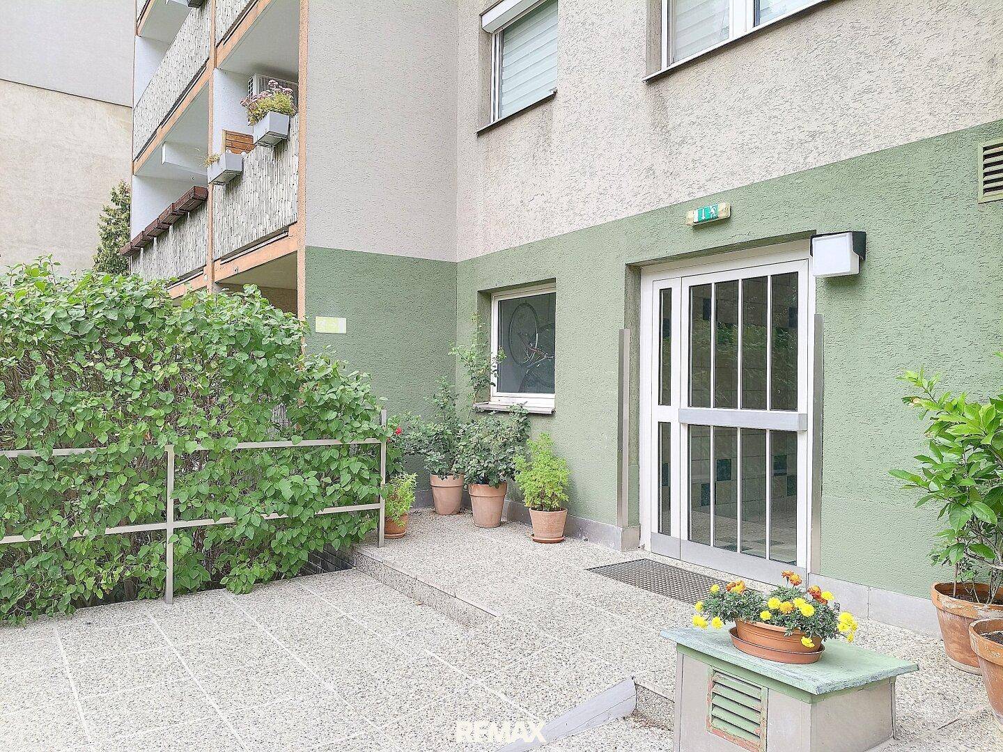 Eingangsbereich des Gebäudes mit Rampe und Topfpflanzen, barrierefrei zugänglich.
