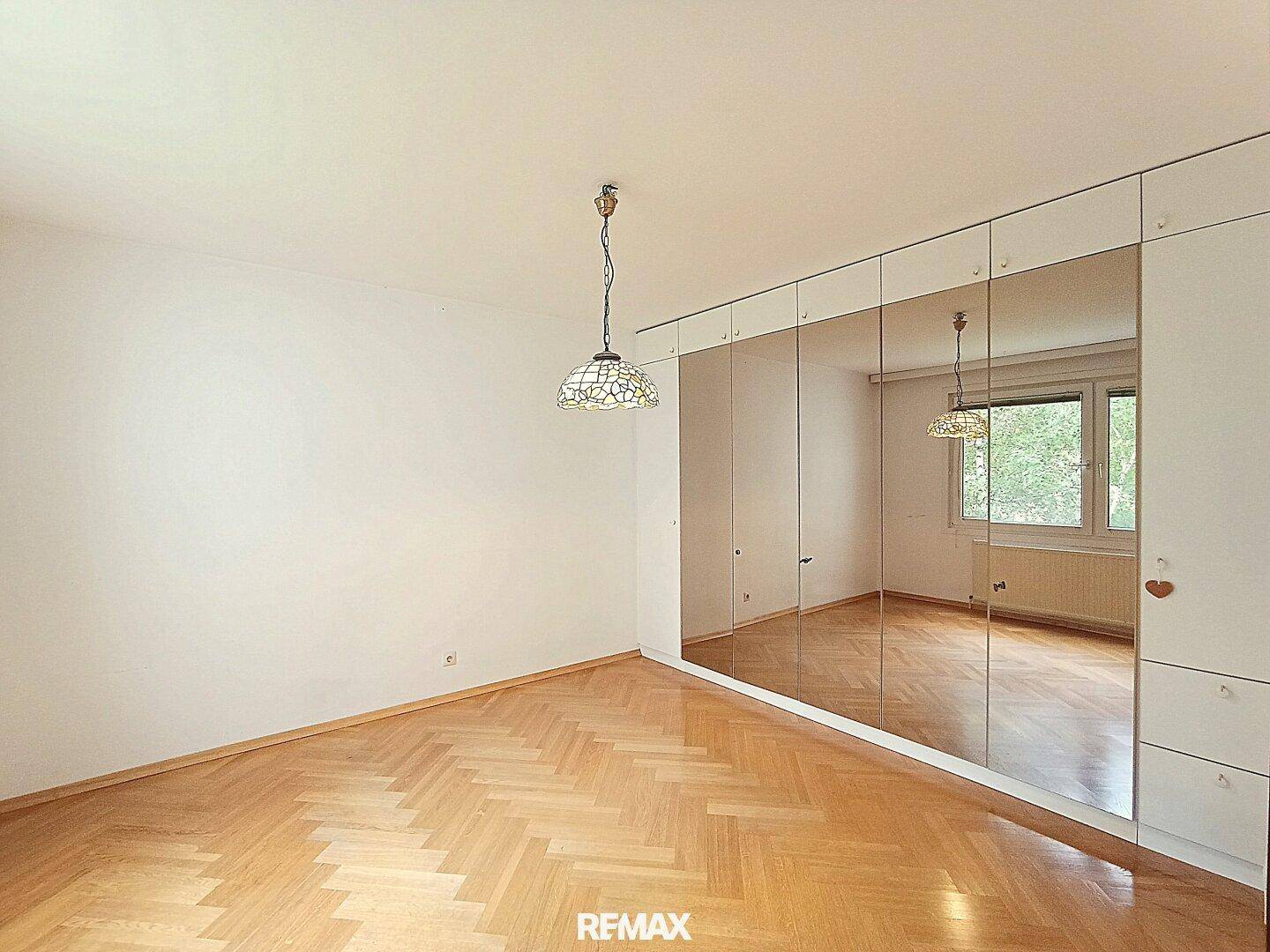 Schlafzimmer mit Fischgrätparkett und einem großen Spiegelschrank, der den Raum optisch vergrößert.