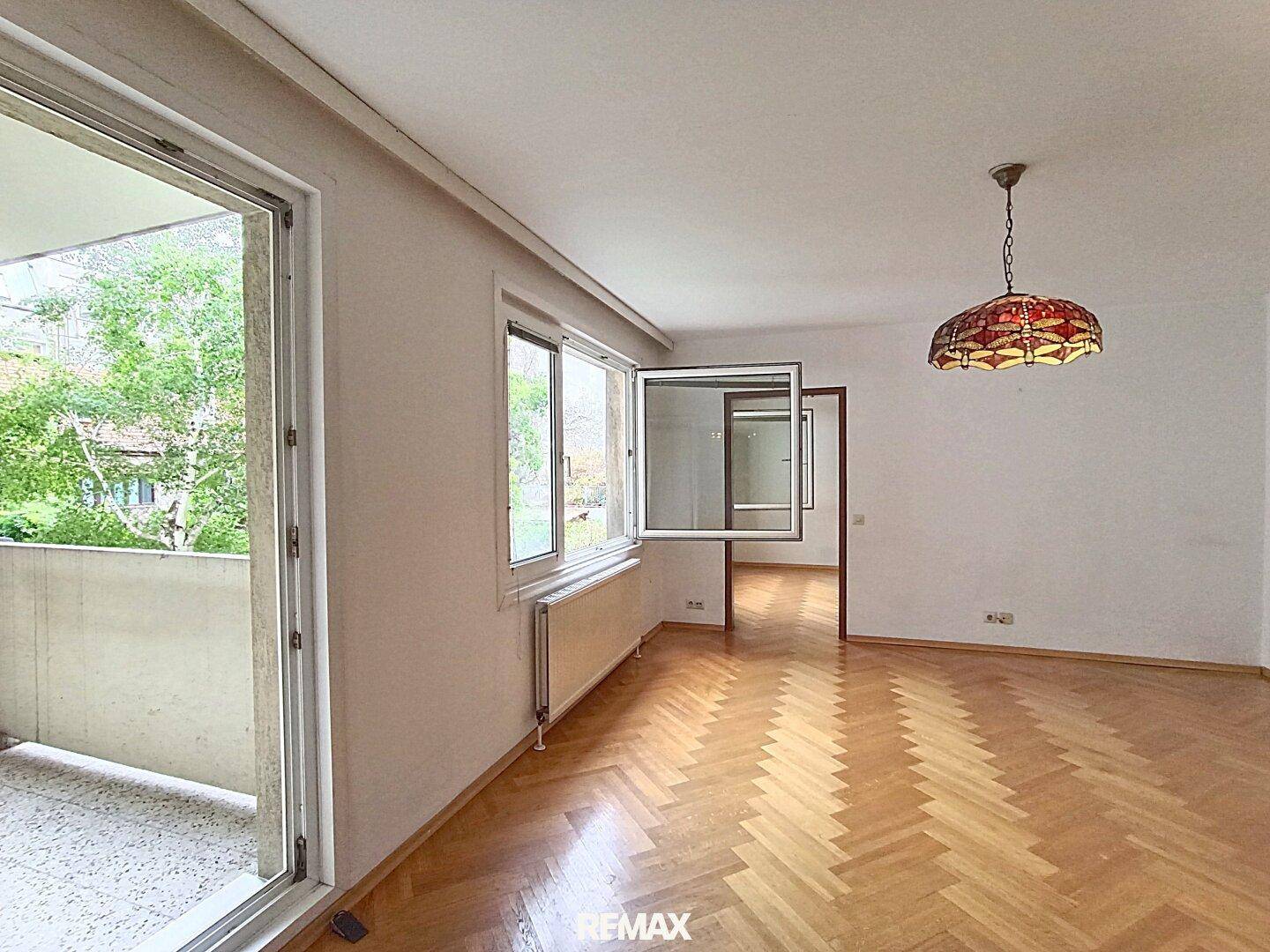 Geräumiges Wohnzimmer mit Parkettboden und großen Fenstern, die viel Tageslicht hereinlassen.