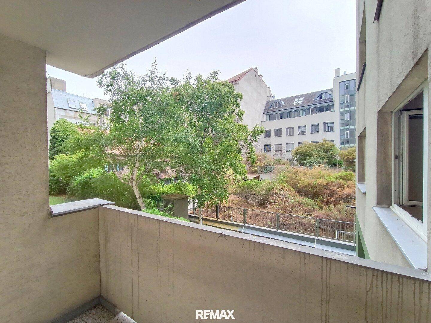 Balkon mit Blick auf einen begrünten Innenhof und umliegende Gebäude, bietet eine ruhige Aussicht.