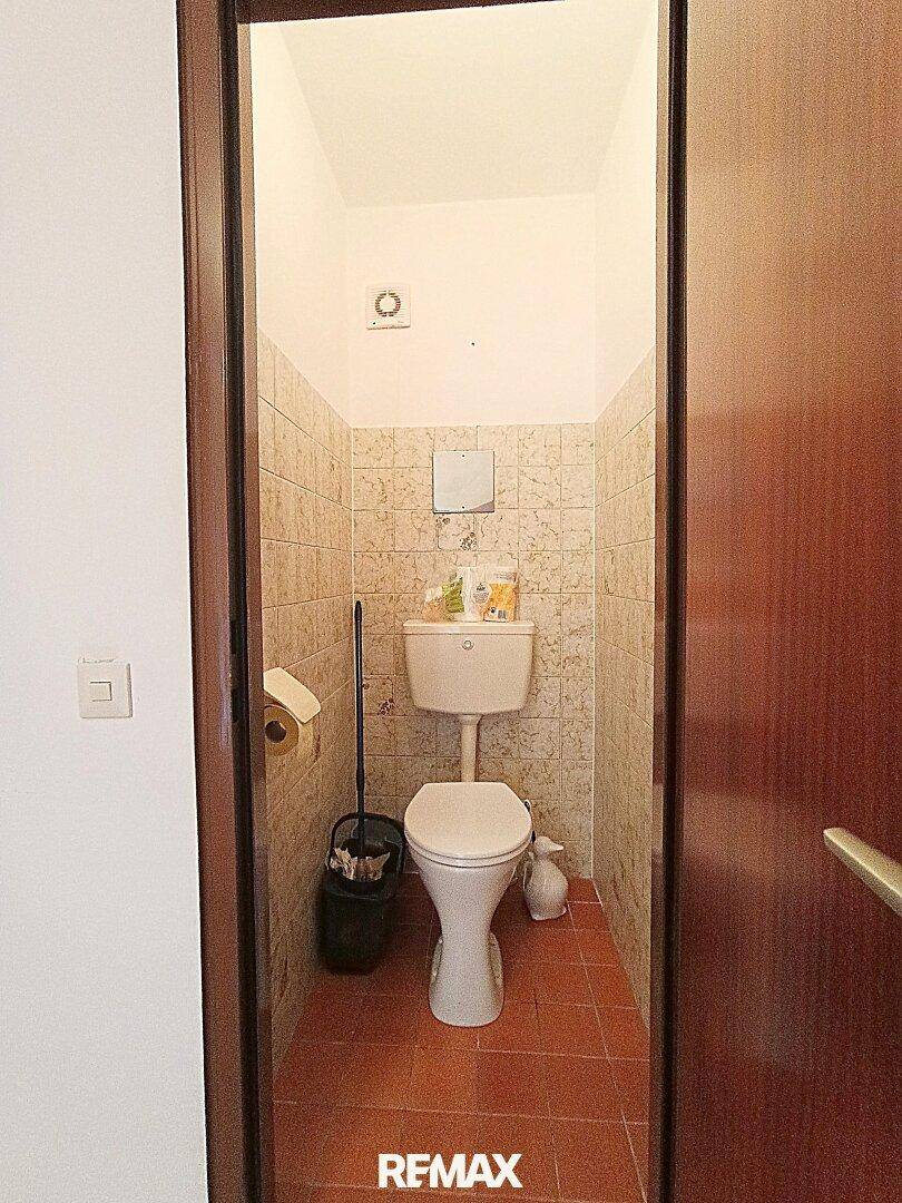 Separates WC mit Fliesen an den Wänden und einem einfachen Stand-WC.