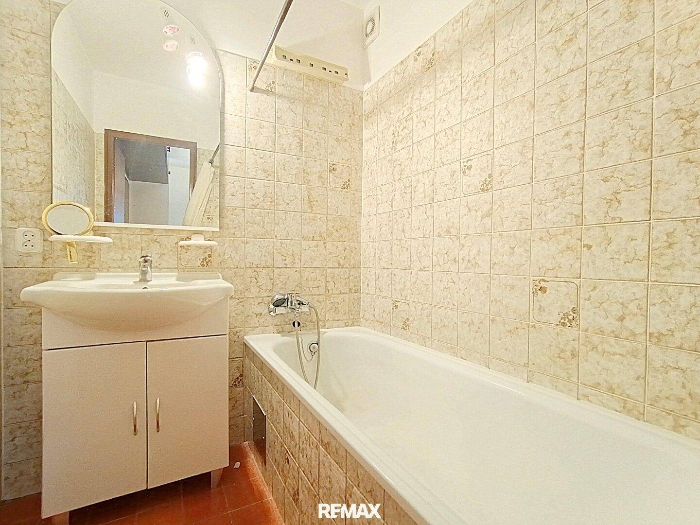 Badezimmer mit Badewanne und hellen Fliesen, ausgestattet mit einem Waschbeckenunterschrank.