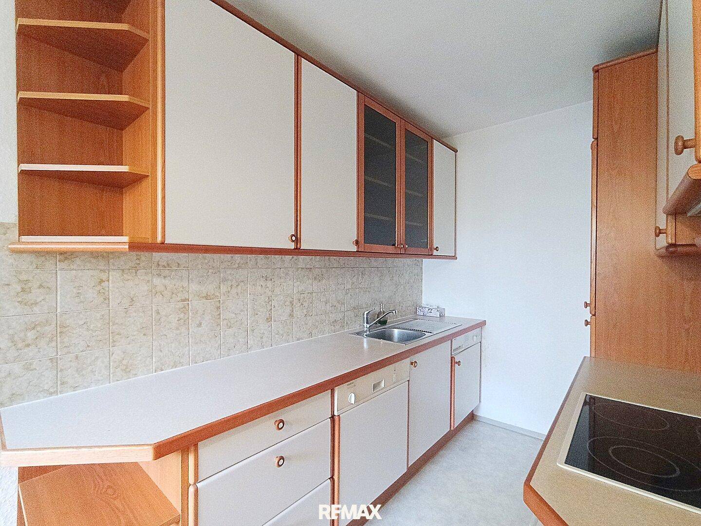 Küchenzeile mit Spüle und Arbeitsfläche, umgeben von hellen Holzschränken und Fliesenrückwand.