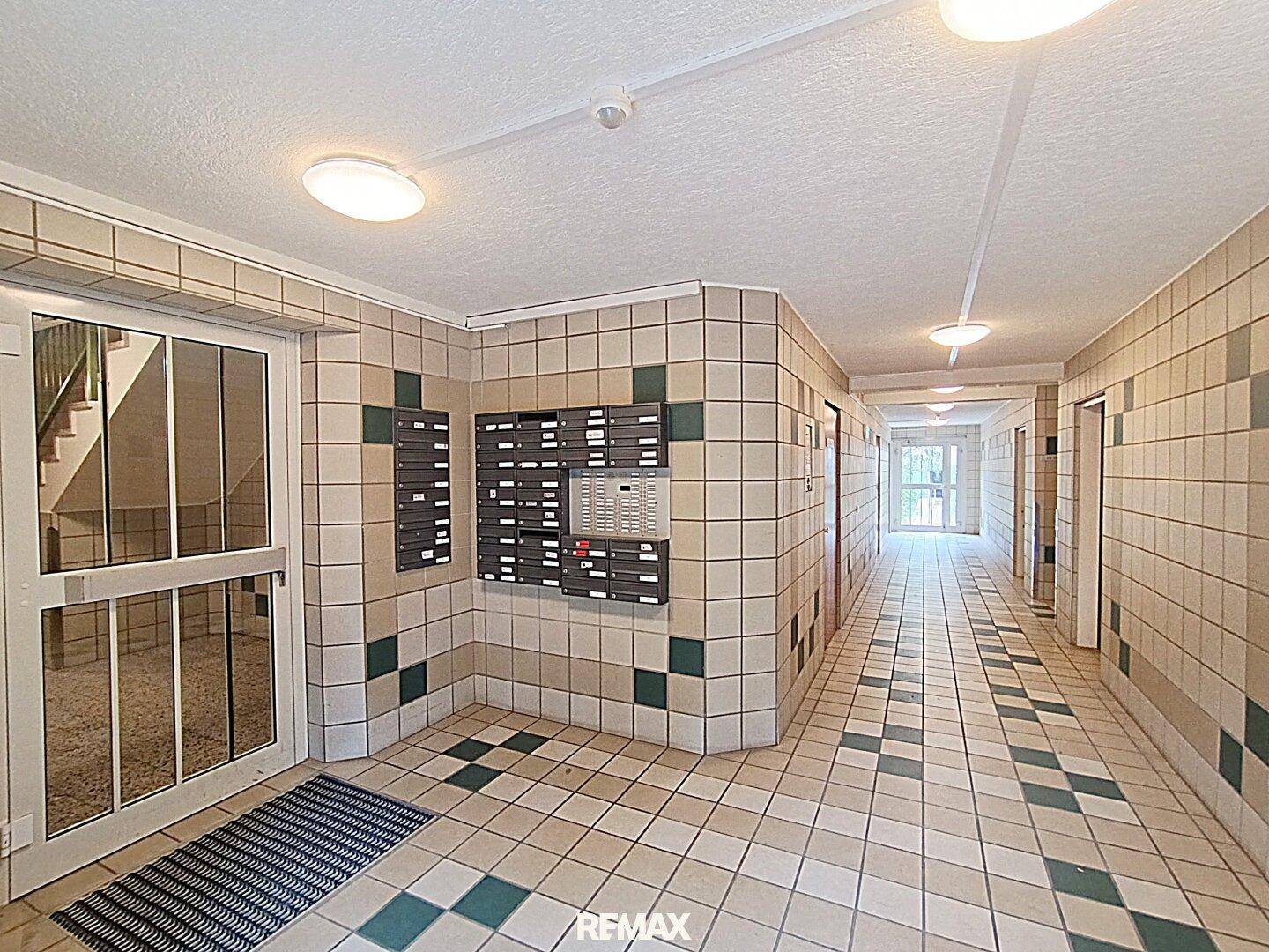 Heller Flur im Gebäude mit Fliesenboden und Briefkästen, führt zu den Wohneinheiten.