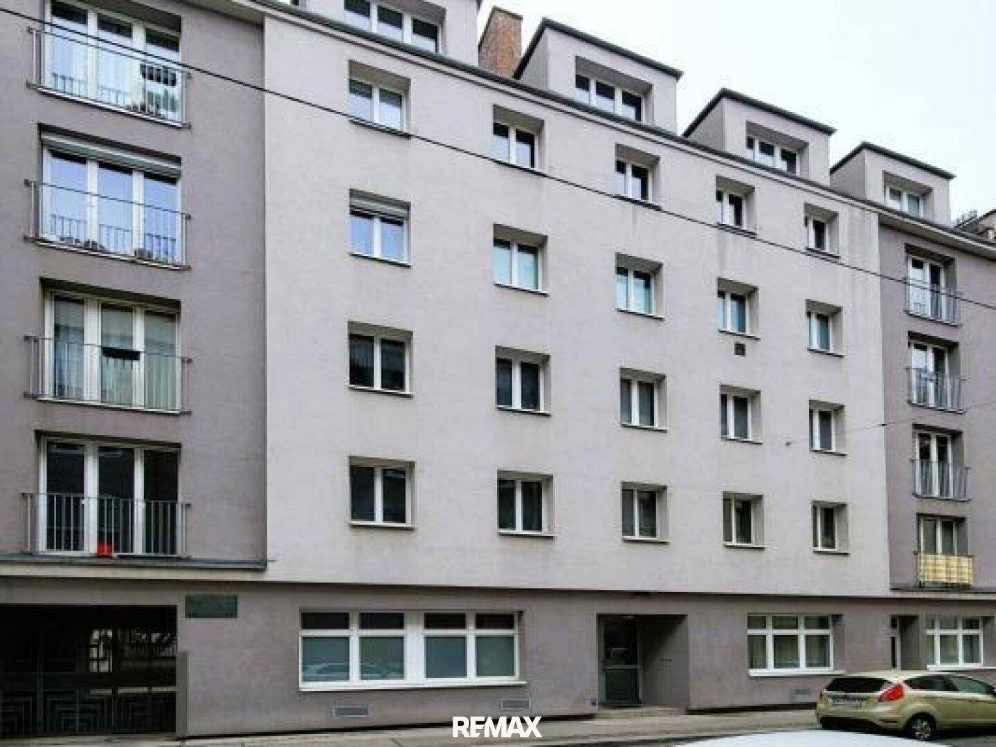 Graue Fassade eines Mehrfamilienhauses mit zahlreichen Fenstern und einigen kleinen Balkonen.