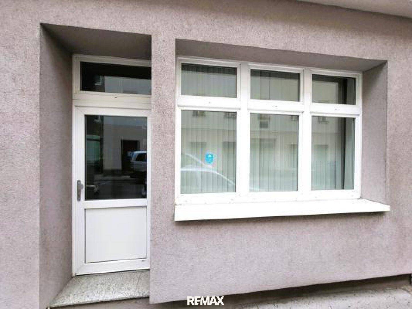Eingangsbereich mit weißer Tür und Fenster in einer grauen Fassade.