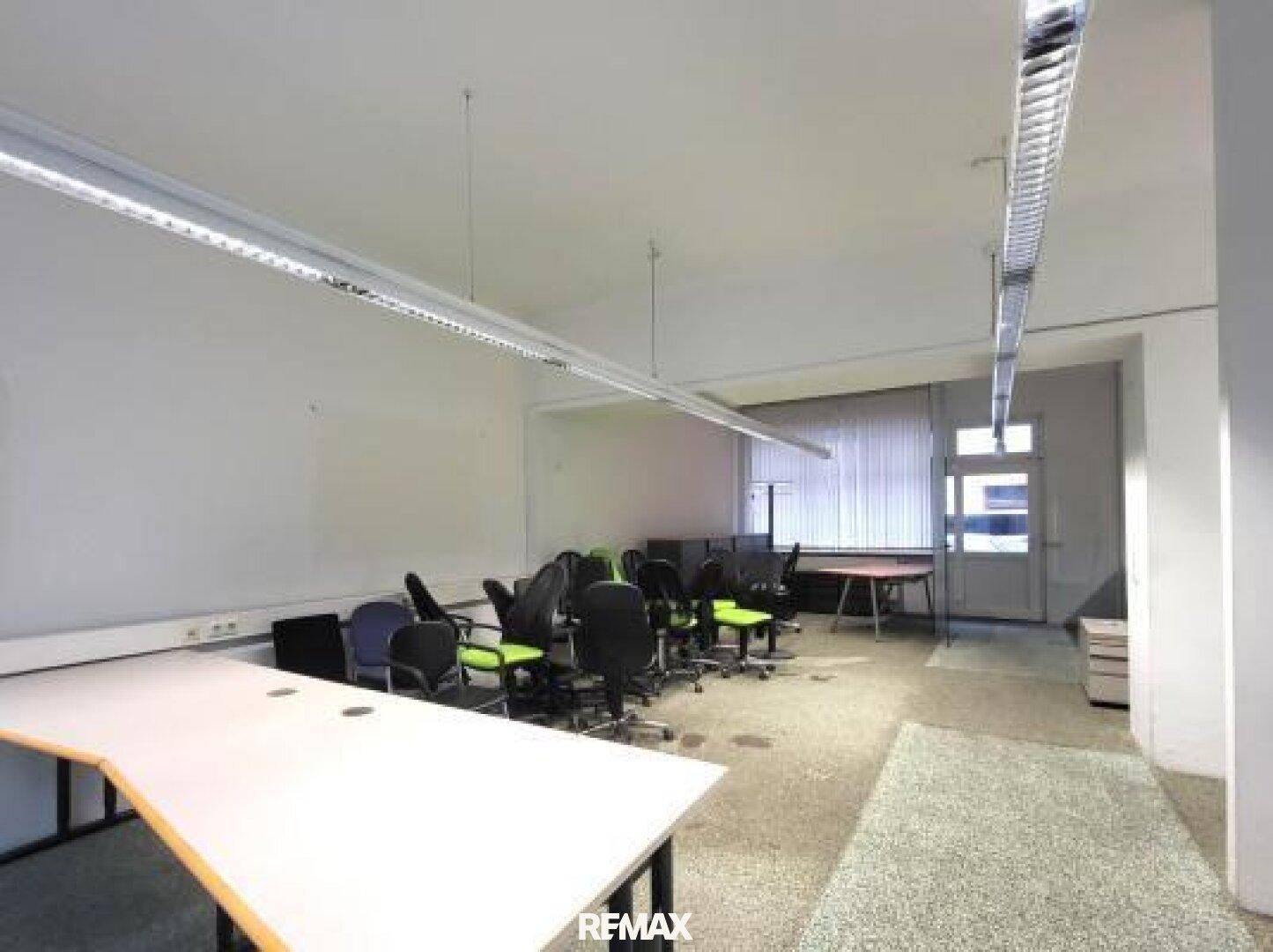 Großer Büroraum mit mehreren Arbeitsplätzen und einer Tür, die nach draußen führt.