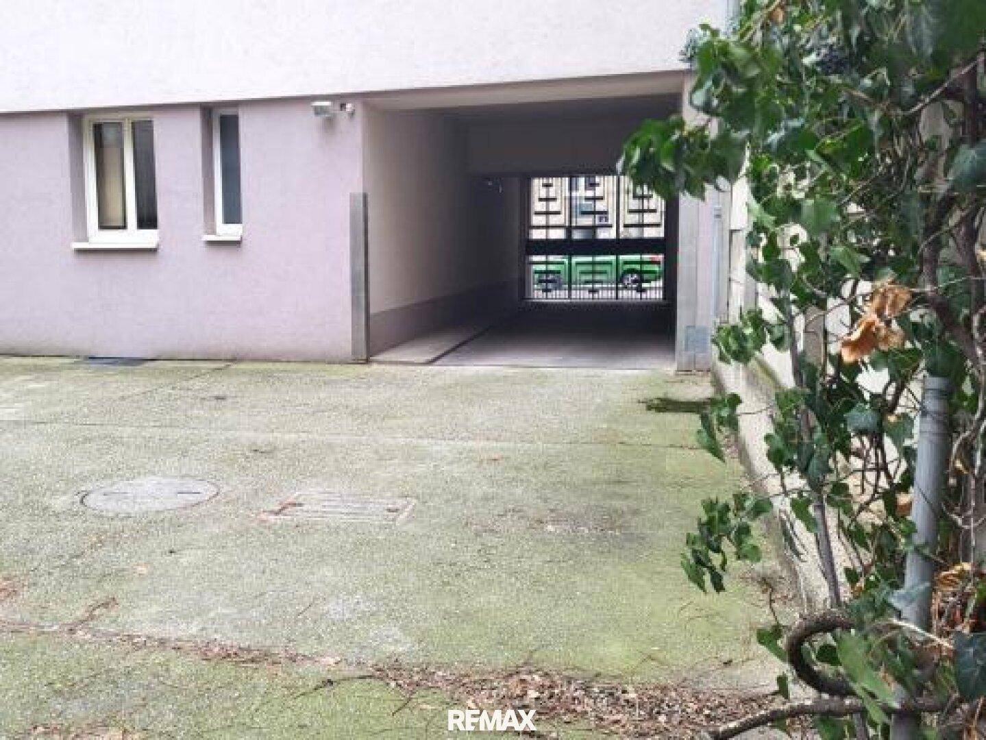 Einfahrt zu einer Tiefgarage oder einem überdachten Parkbereich mit Blick auf ein Gittertor.