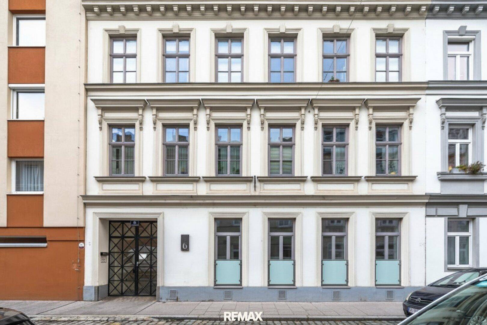 Historische Fassade eines Altbaus mit eleganten Verzierungen, großen Fenstern und französischen Balkonen im Erdgeschoss.
