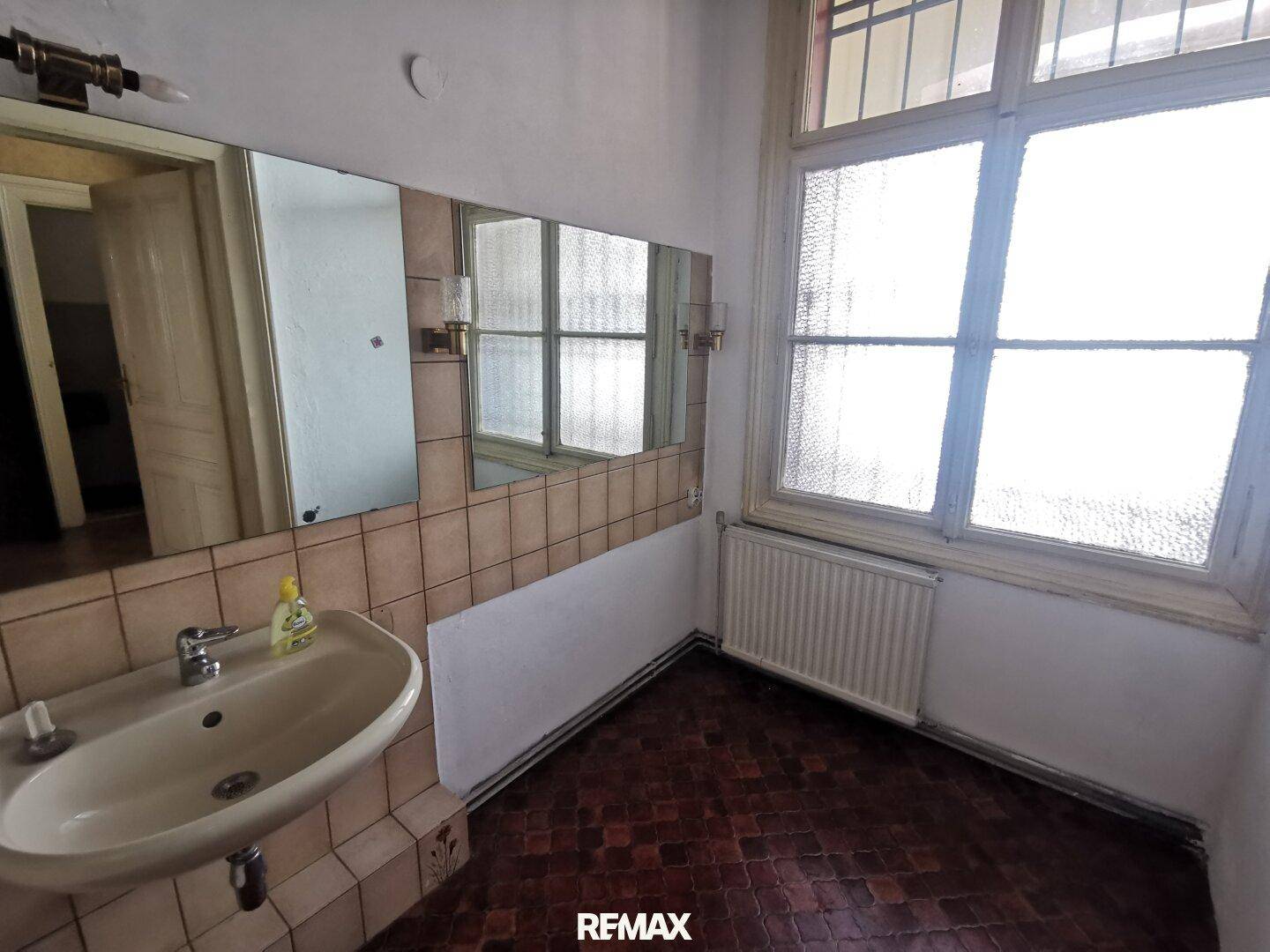 Badezimmer mit Waschbecken, großem Spiegel und Fenster, das viel Tageslicht hereinlässt.