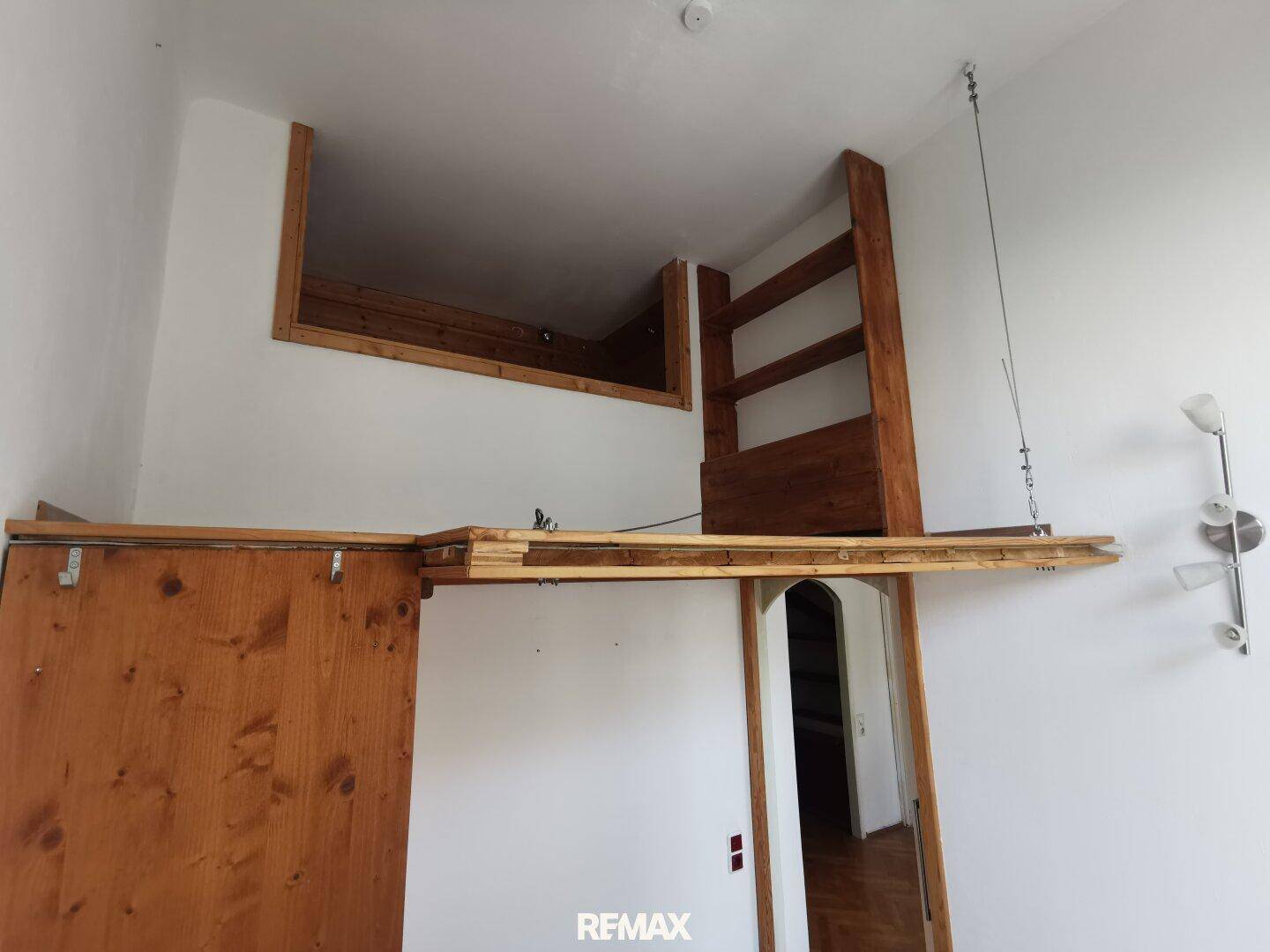 Zimmer mit Hochbettkonstruktion aus Holz und hoher Decke, bietet zusätzlichen Schlaf- oder Stauraum.