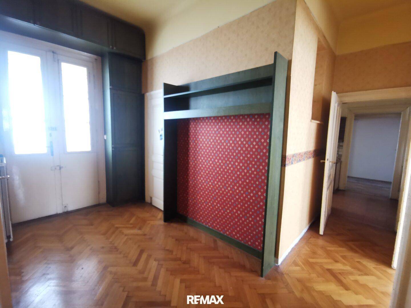 Geräumiges Zimmer mit Fischgrätparkett und Zugang zu einem Balkon, bietet viel Potenzial.
