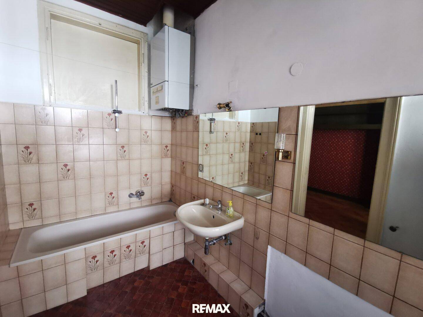 Badezimmer mit Badewanne, Waschbecken und Wandfliesen im Vintage-Stil, renovierungsbedürftig.