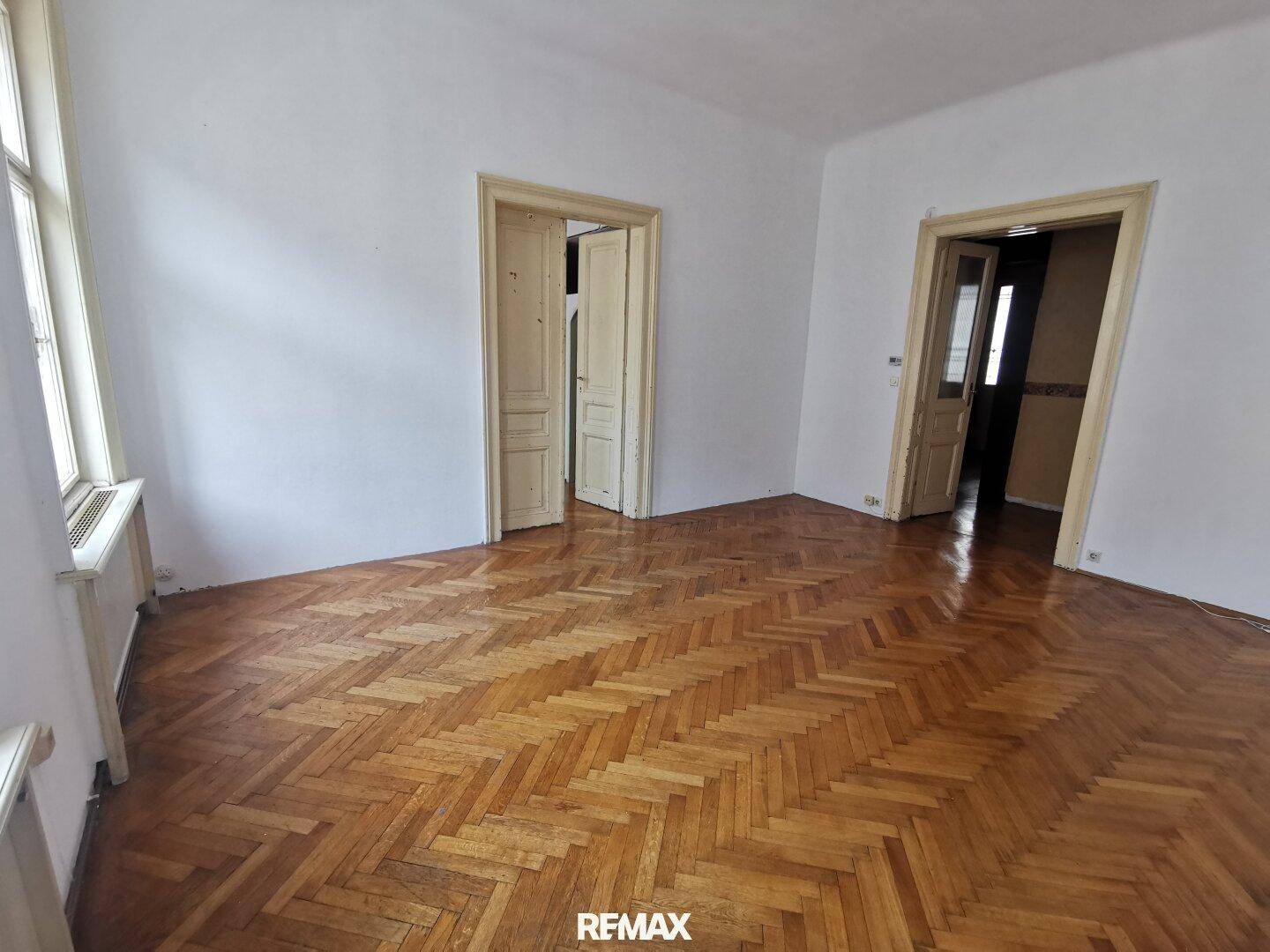 Geräumiges Zimmer mit klassischem Fischgrätparkett und zwei Holztüren, bereit zur individuellen Gestaltung.