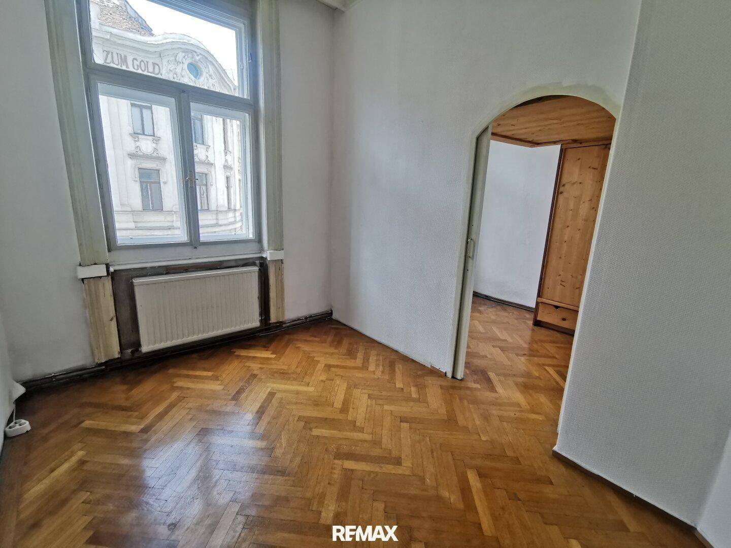Gemütliches Zimmer mit Fischgrätparkett, großem Fenster und Blick auf die Stadt, ideal als Schlafzimmer.