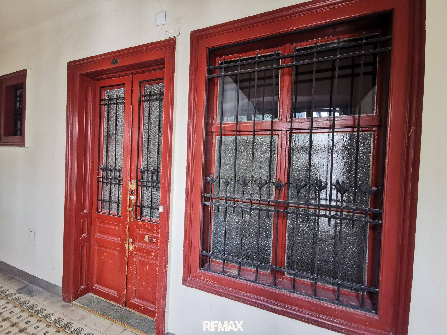 Rote Eingangstür und Fenster mit schmiedeeisernen Gittern, die den historischen Charme betonen.
