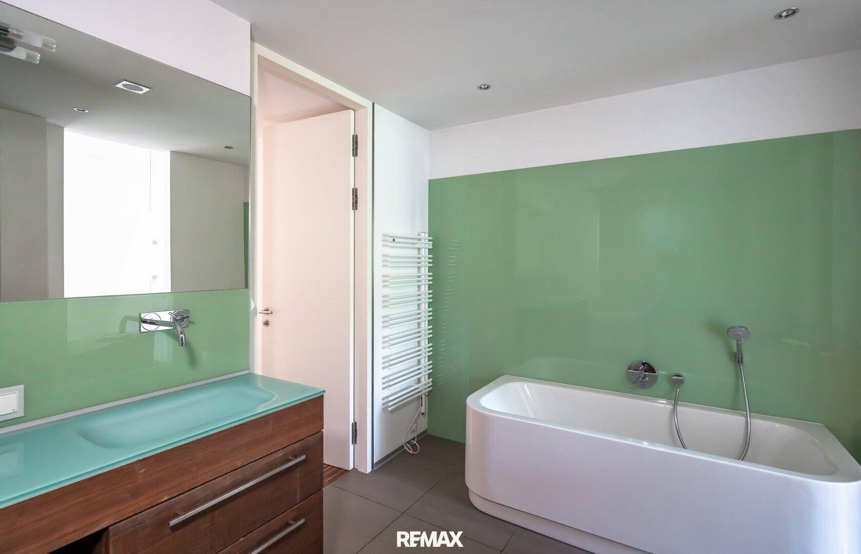 Modernes Badezimmer mit Badewanne, Einzelwaschbecken und grünen Wandpaneelen.