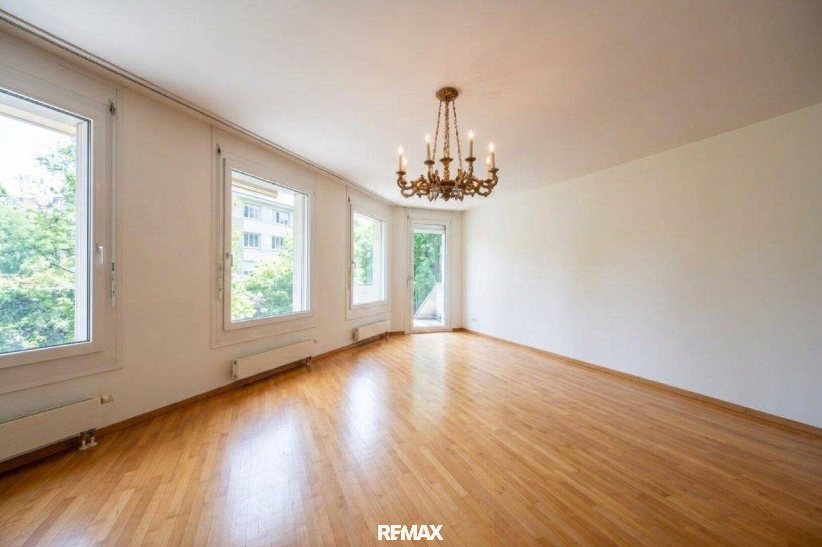 Heller Wohnbereich mit Parkettboden, Kronleuchter und Zugang zu einem möglichen Balkon oder einer Terrasse.