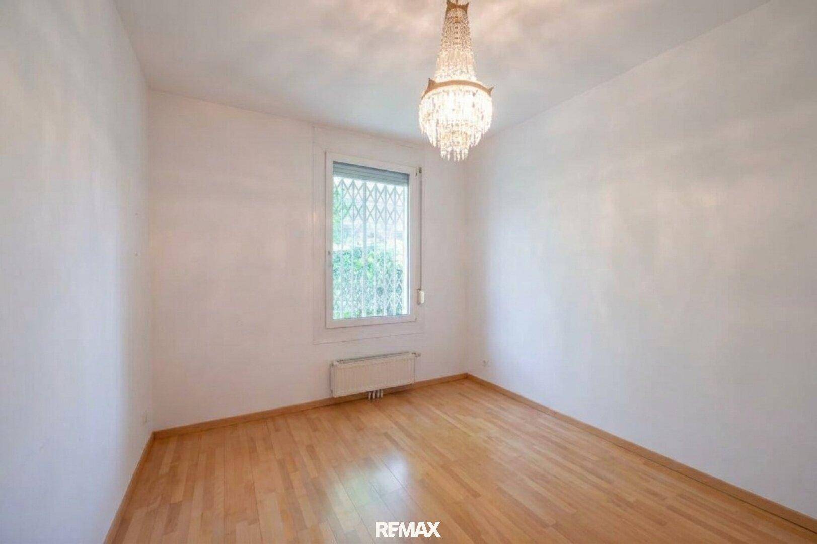 Helles Zimmer mit Parkettboden, einem Fenster mit Rollladen und einem dekorativen Kronleuchter.