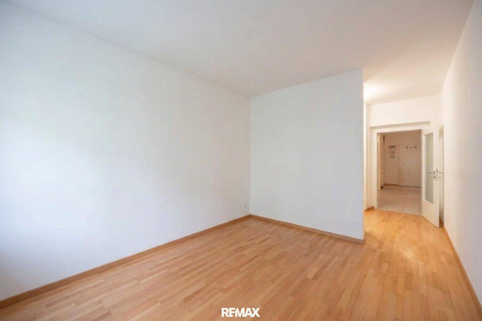 Leeres Zimmer mit Parkettboden und Zugang zum gefliesten Flur, ideal als Schlaf- oder Arbeitszimmer.