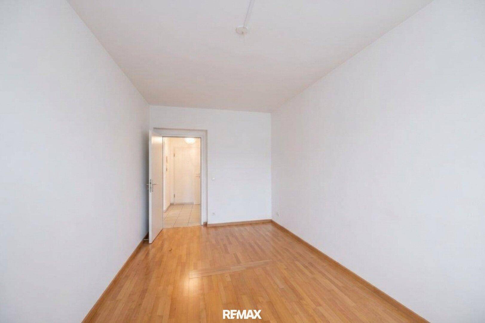 Helles Zimmer mit Parkettboden und einer Tür, die zu einem anderen Bereich der Wohnung führt.