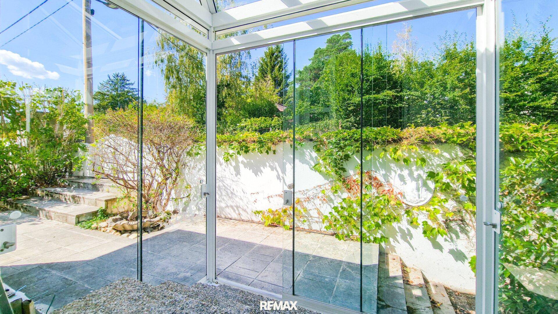 Heller Wintergarten mit Glaswänden bietet einen schönen Blick auf die Terrasse und den grünen Garten.