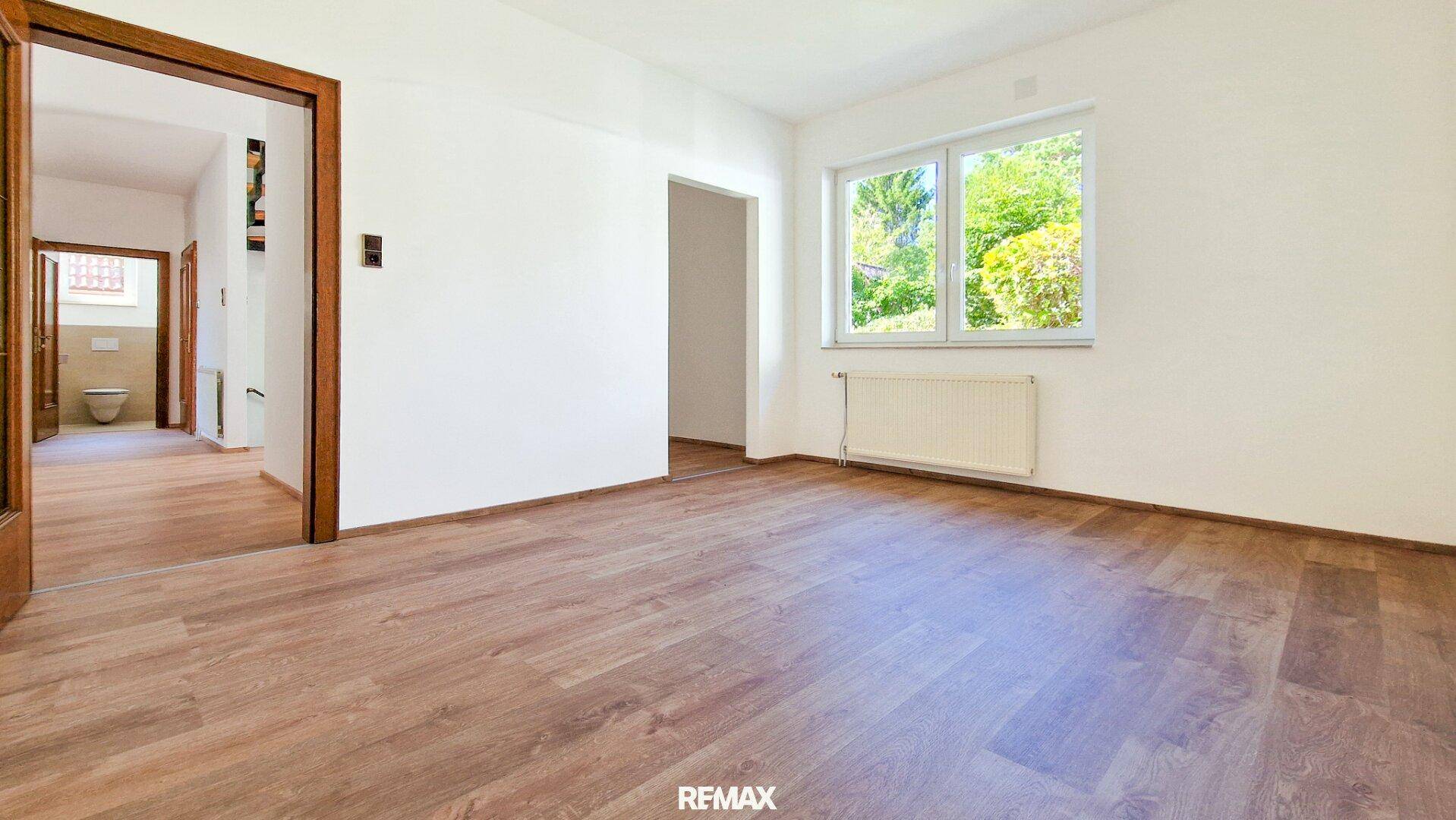 Heller Raum mit Holzboden, weißen Wänden und einem Fenster, das viel Tageslicht hereinlässt.