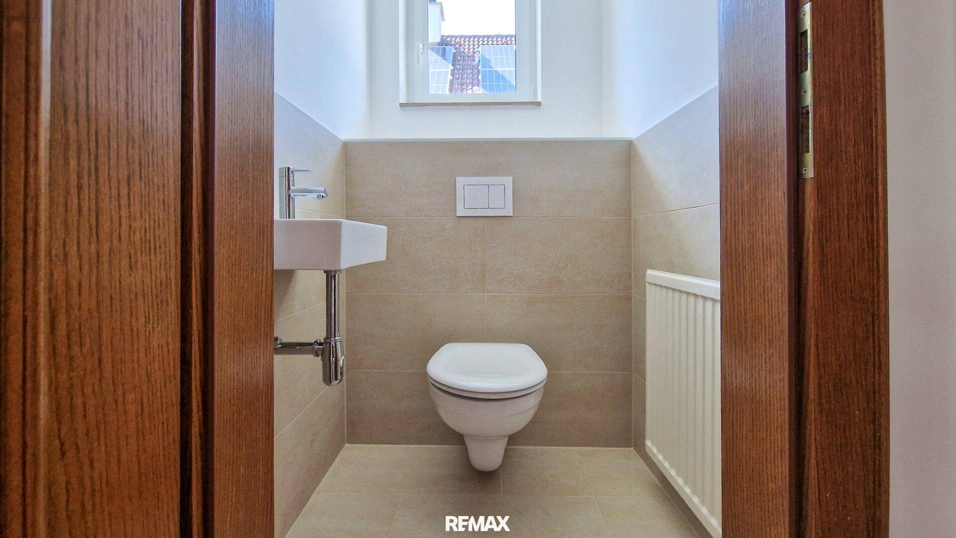 Modernes Gäste-WC mit wandhängender Toilette, kleinem Waschbecken und einem Fenster.