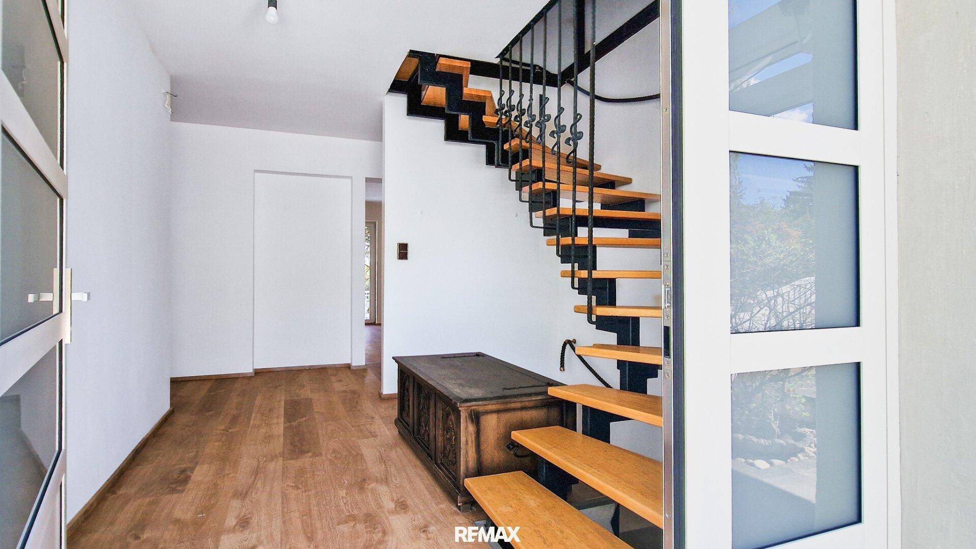 Eingangsbereich mit eleganter Holztreppe, Holzboden und einem antiken Möbelstück.