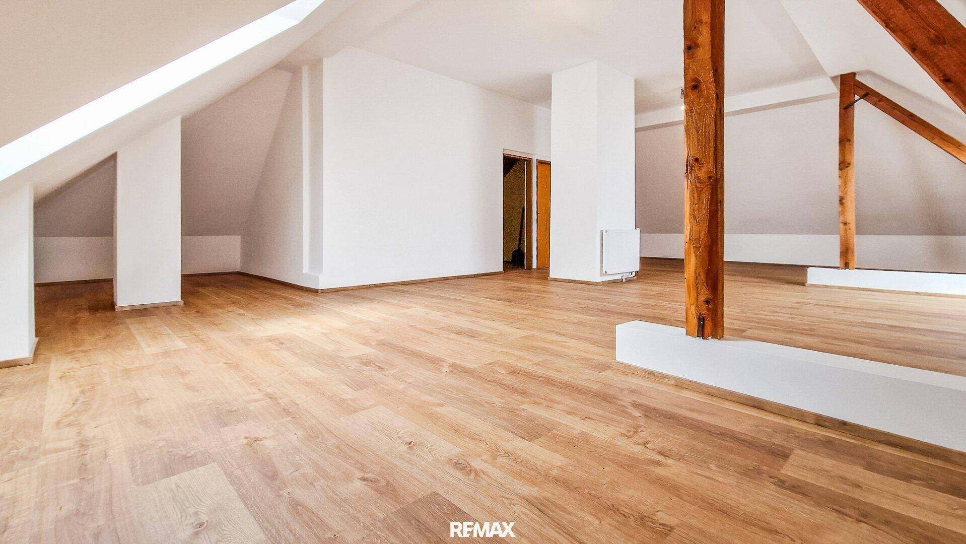 Geräumiger Dachbodenraum mit Holzboden, weißen Wänden und sichtbaren Holzbalken unter der Dachschräge.