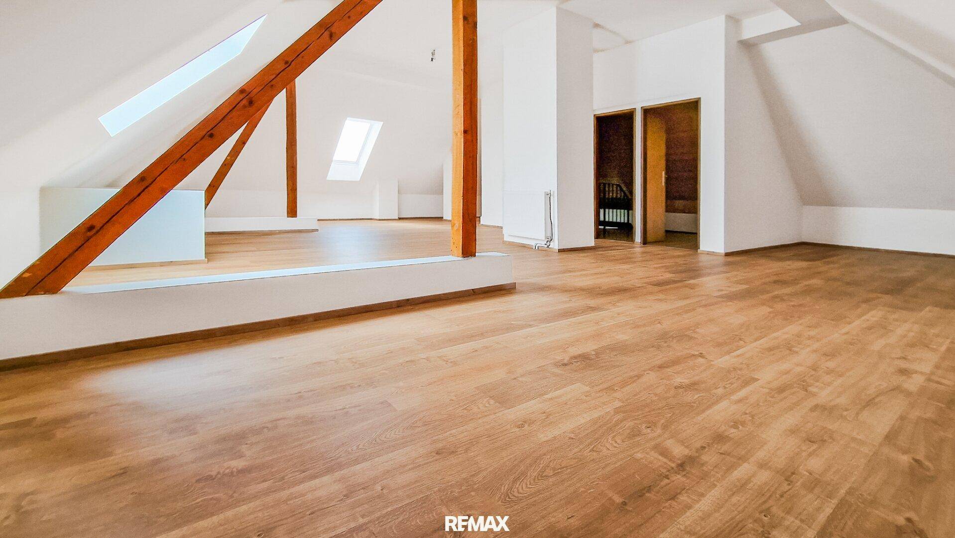 Heller Dachbodenraum mit Holzboden, sichtbaren Holzbalken und Dachfenstern für natürliches Licht.