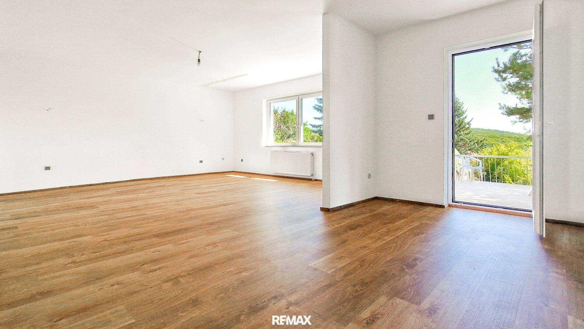 Heller, leerer Wohnbereich mit Holzboden, weißen Wänden und Zugang zu einer Außenterrasse.
