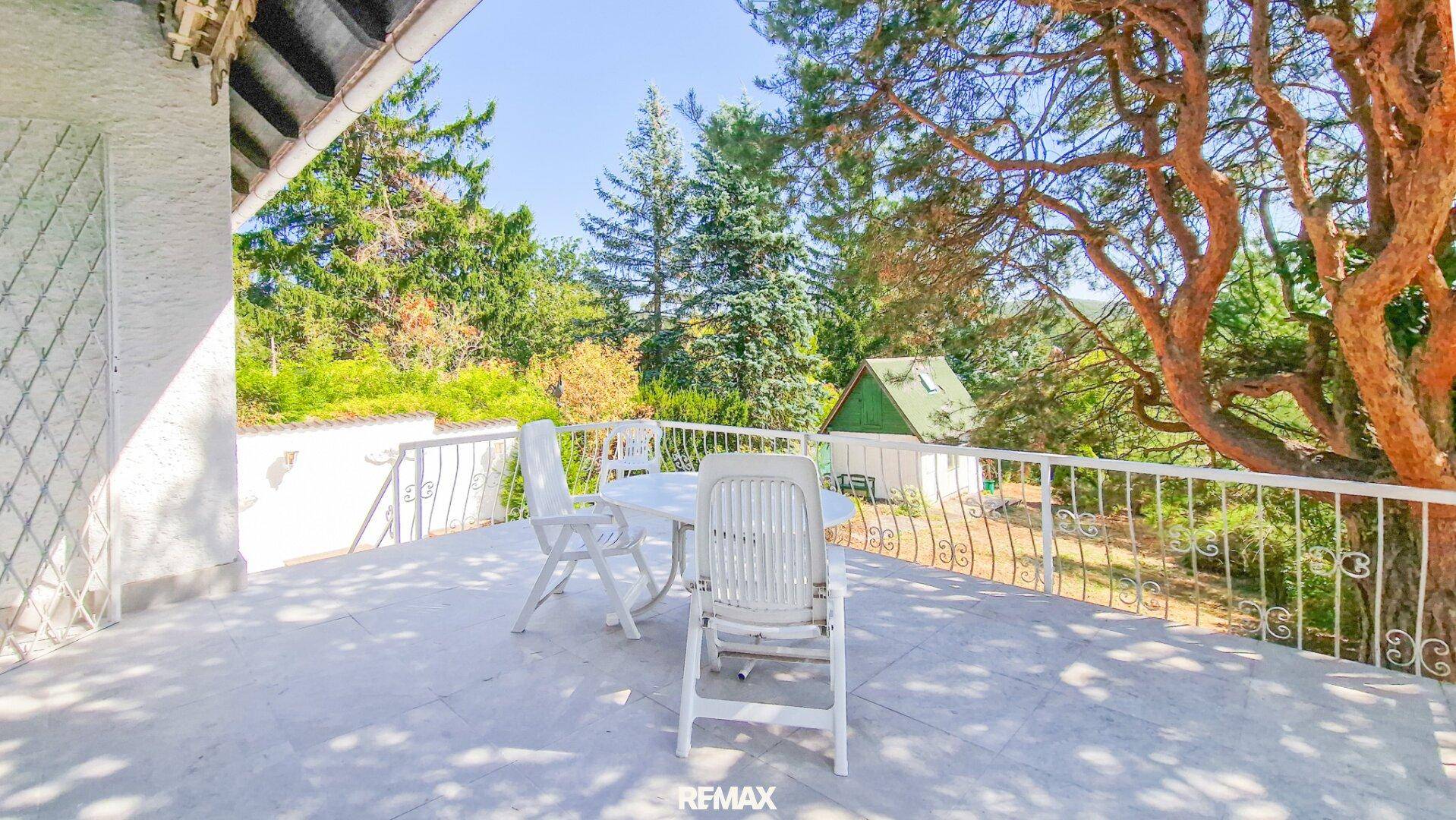 Geräumige Terrasse mit weißen Gartenmöbeln und weitem Blick ins Grüne unter blauem Himmel.