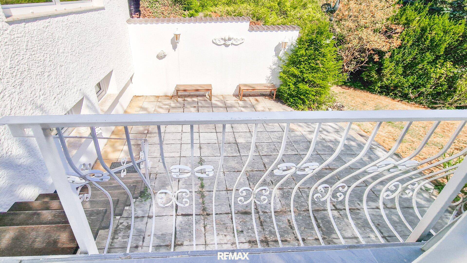 Gepflasterte Terrasse mit dekorativem Geländer und einer weißen Mauer im Hintergrund.
