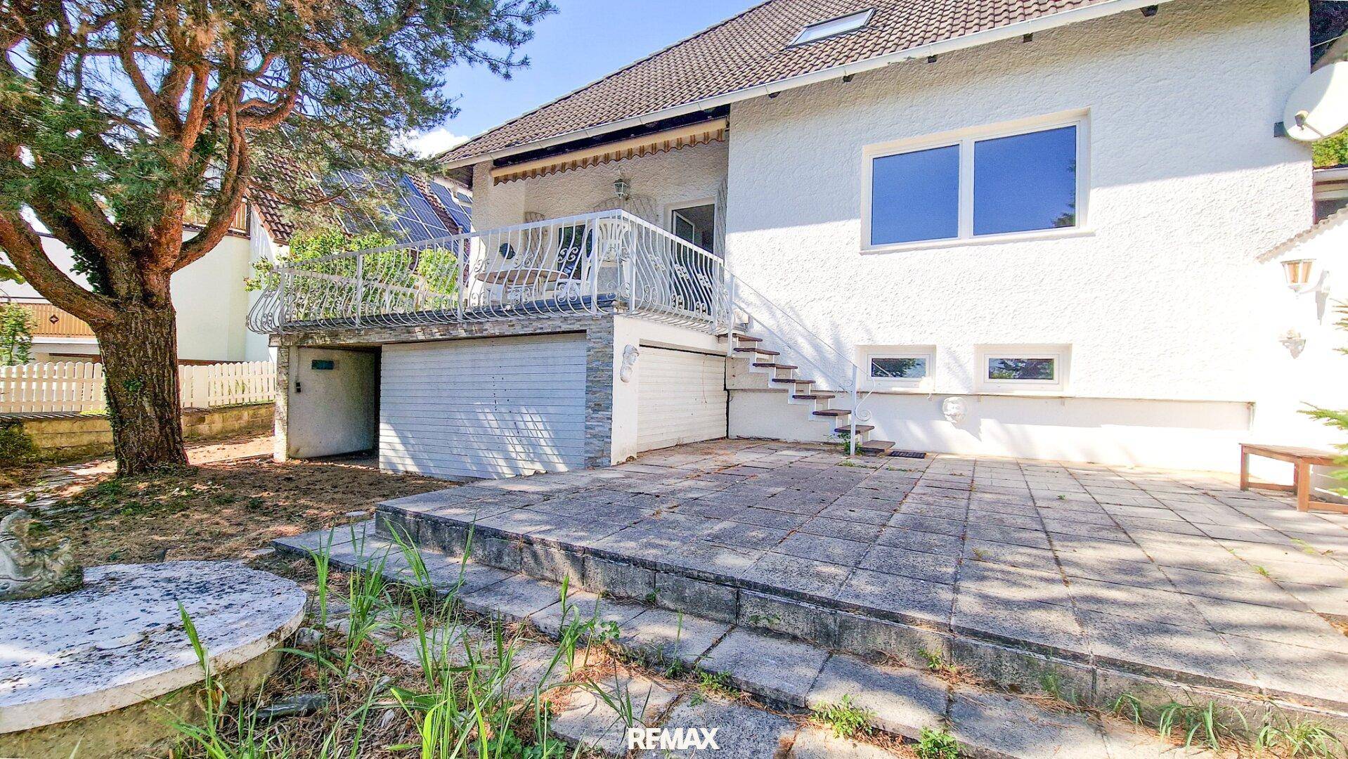 Rückseite des Hauses mit großer gepflasterter Terrasse, Balkon und integrierter Garage.