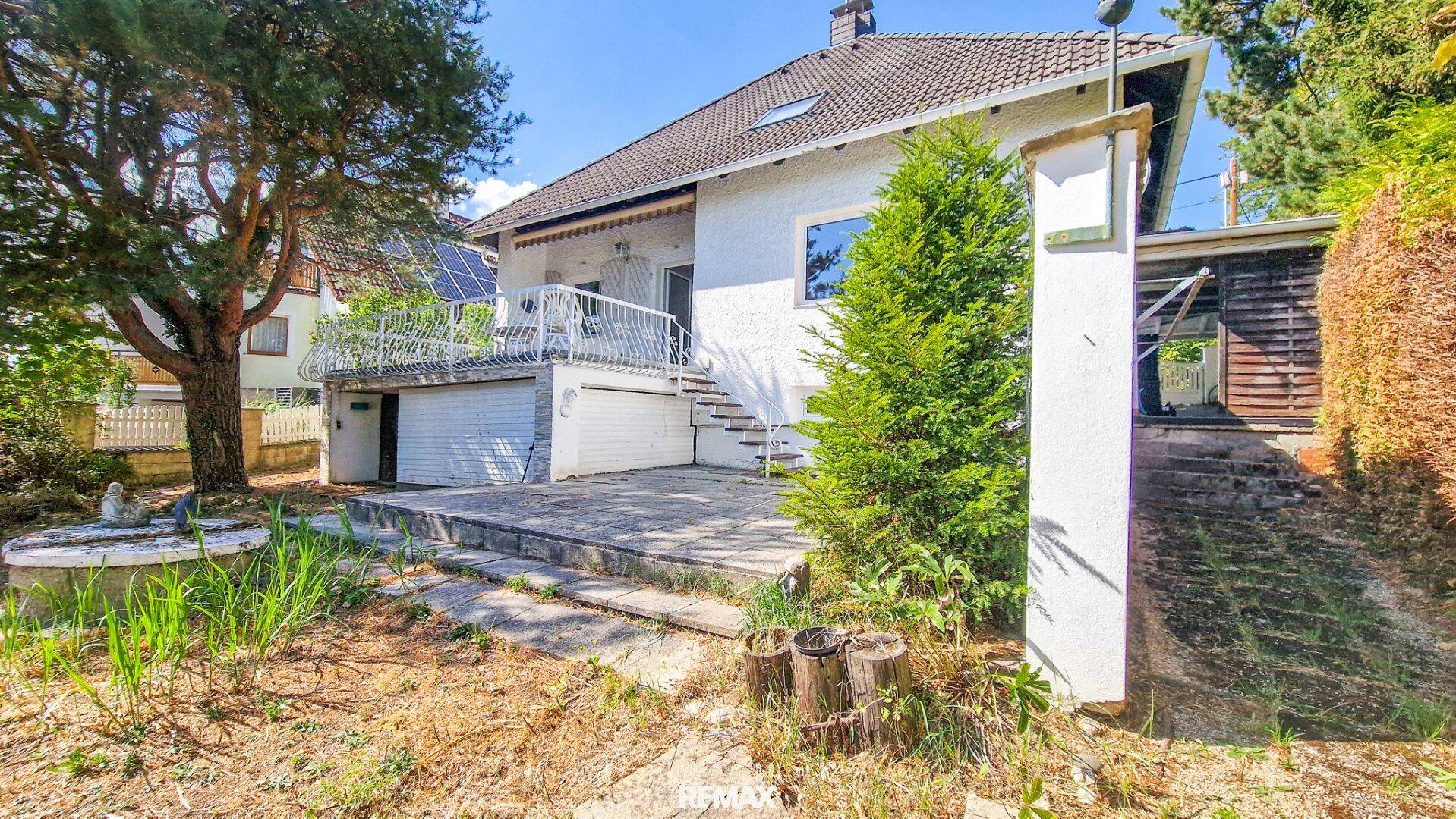 Rückansicht des Hauses mit Terrasse, Balkon und einem kleinen Baum im Vordergrund.