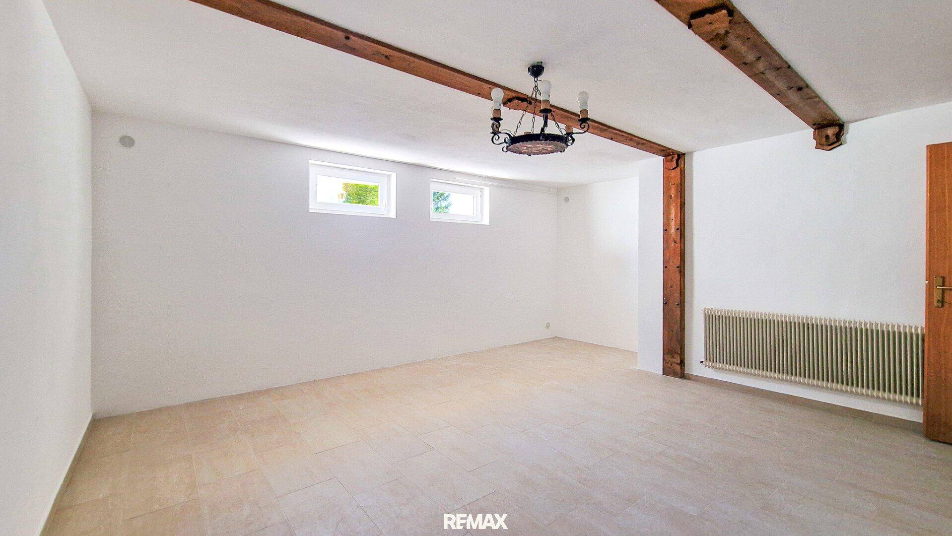 Heller Kellerraum mit sichtbaren Holzbalken an der Decke und kleinen Fenstern.
