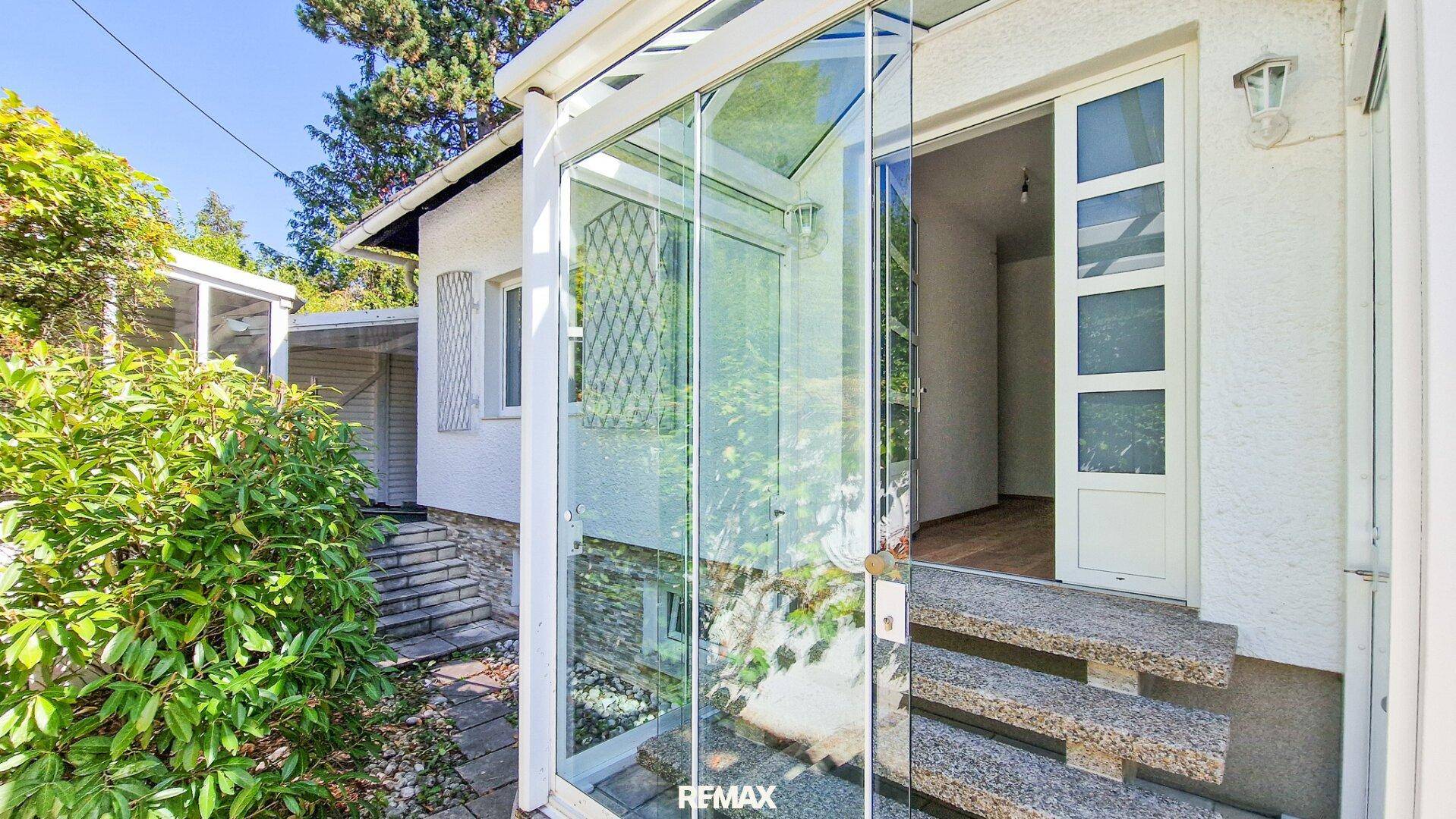 Eingangsbereich des Hauses mit einer modernen Glasüberdachung und Steinstufen.