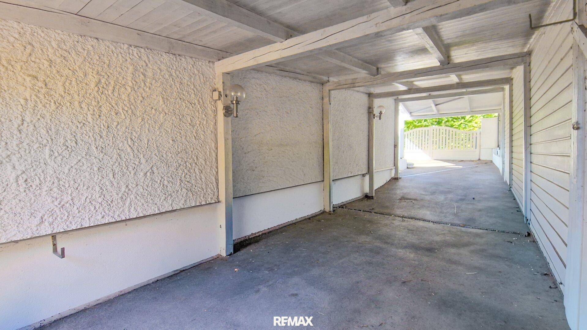 Überdachter Bereich neben dem Haus mit strukturierten Wänden und Deckenbalken.