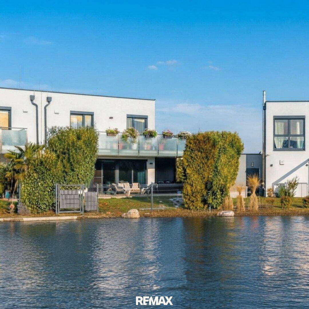 Moderne weiße Gebäude am Wasser mit Balkonen und gepflegter Außenanlage unter blauem Himmel.
