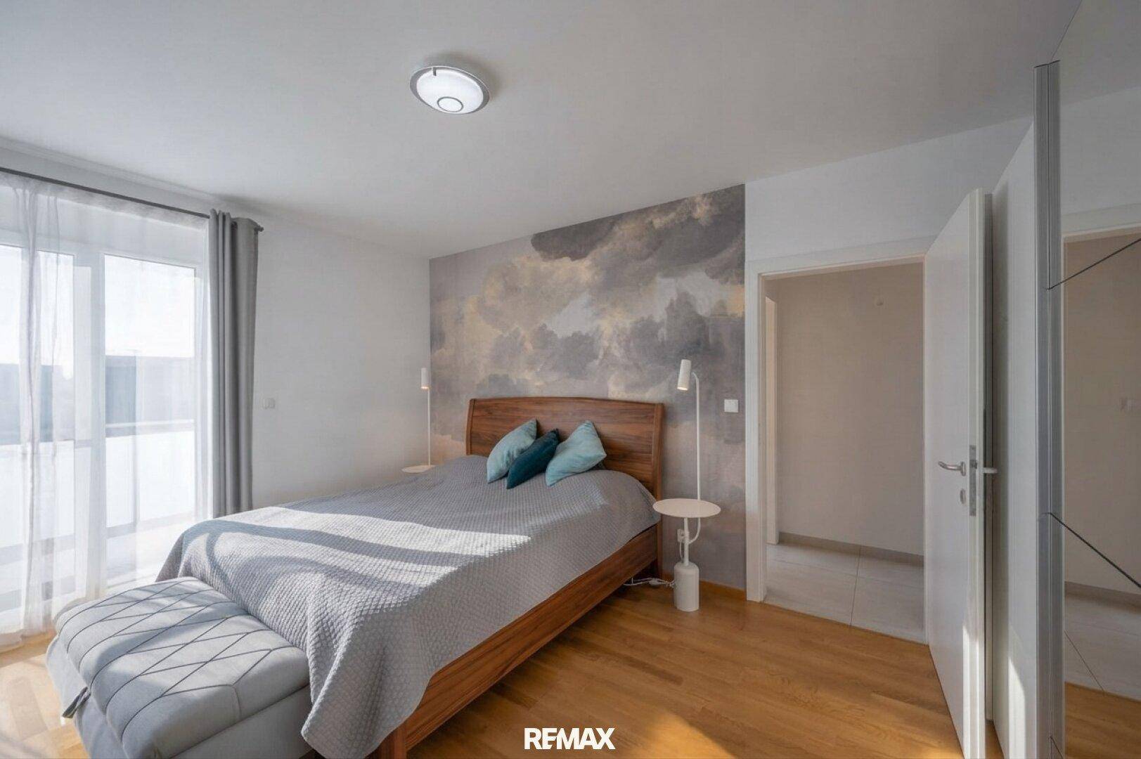 Helles Schlafzimmer mit Holzbett, dekorativer Wandgestaltung und Zugang zu einem Balkon.