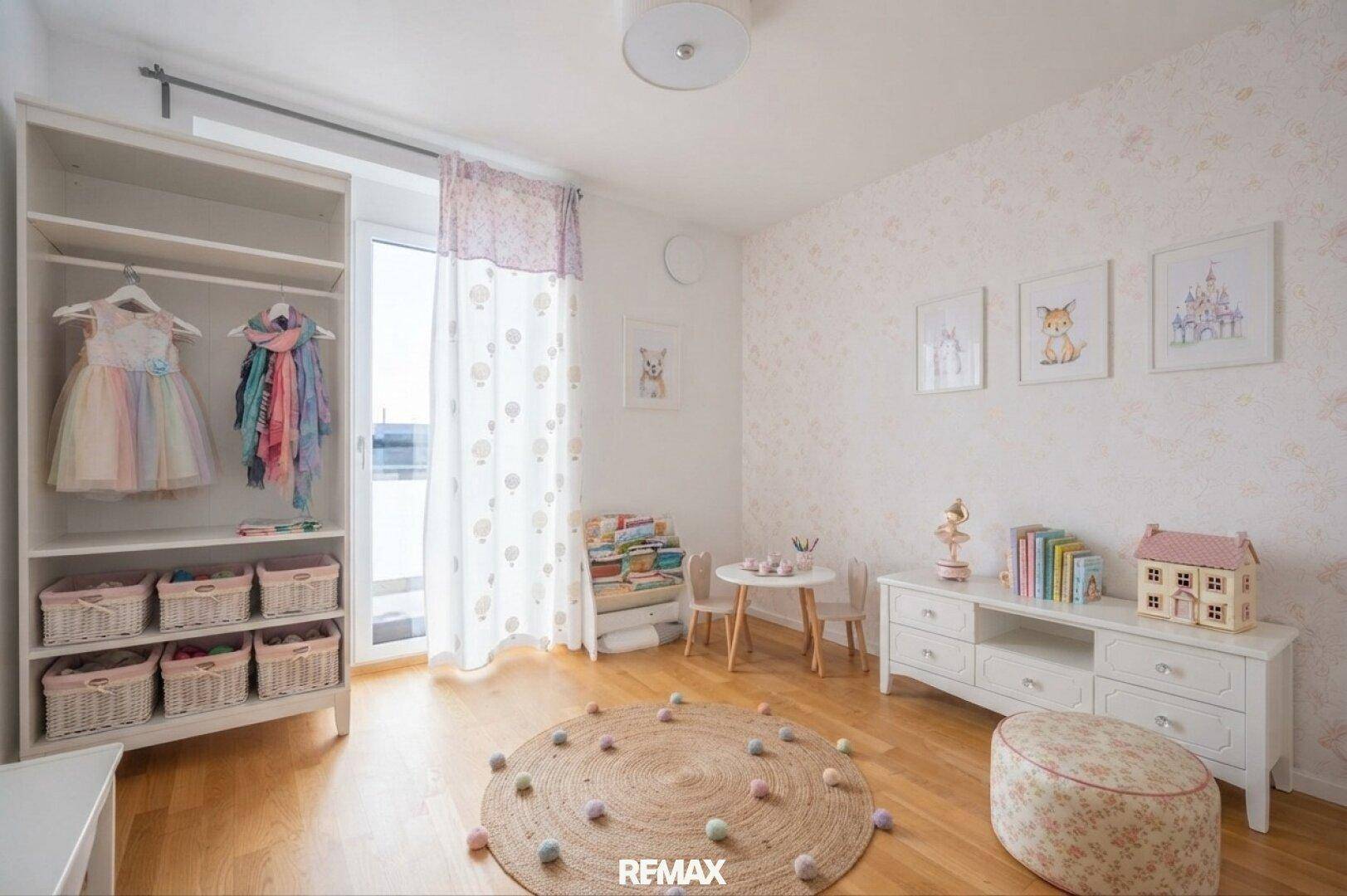 Freundliches Kinderzimmer mit floraler Tapete, Holzboden und offenem Kleiderschrank für Kinderkleidung.
