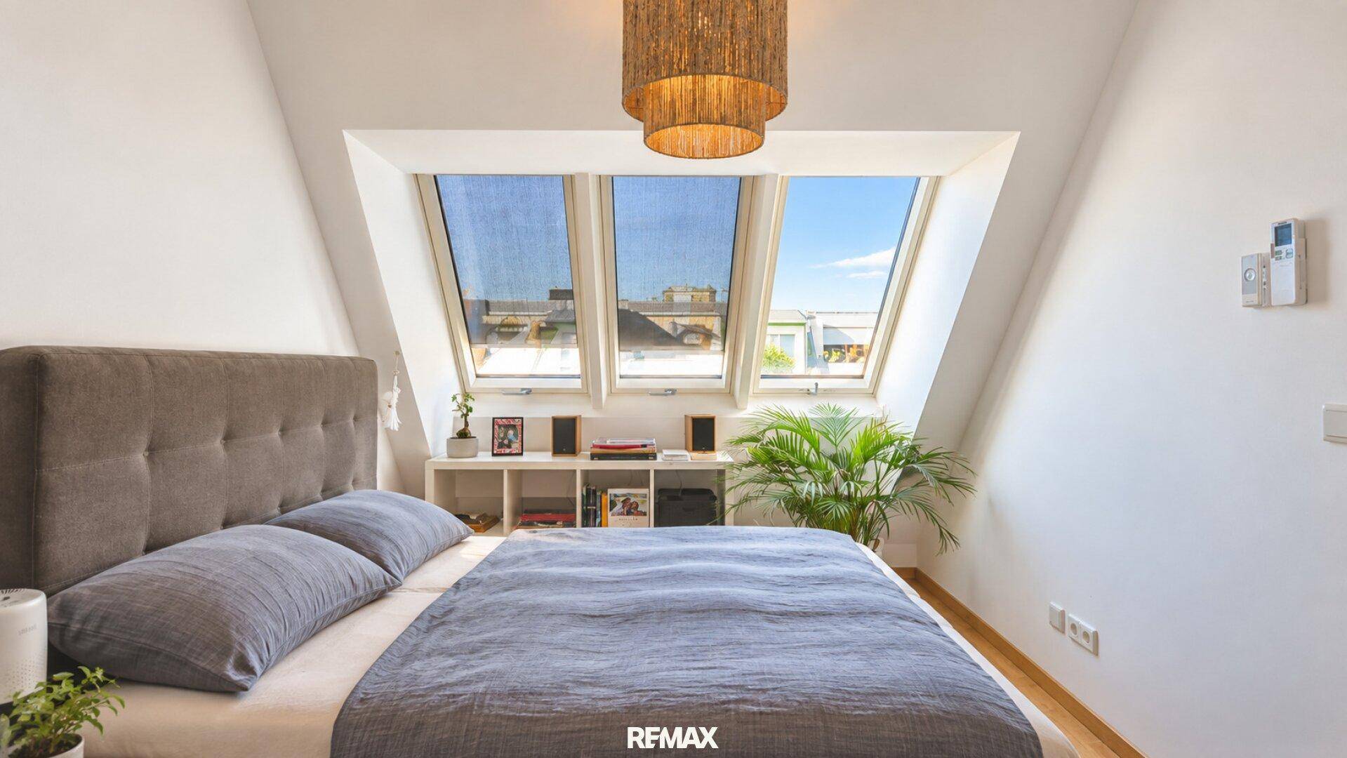 Schlafzimmer im Dachgeschoss mit schrägen Wänden, Holzboden und großen Dachfenstern für viel Licht.